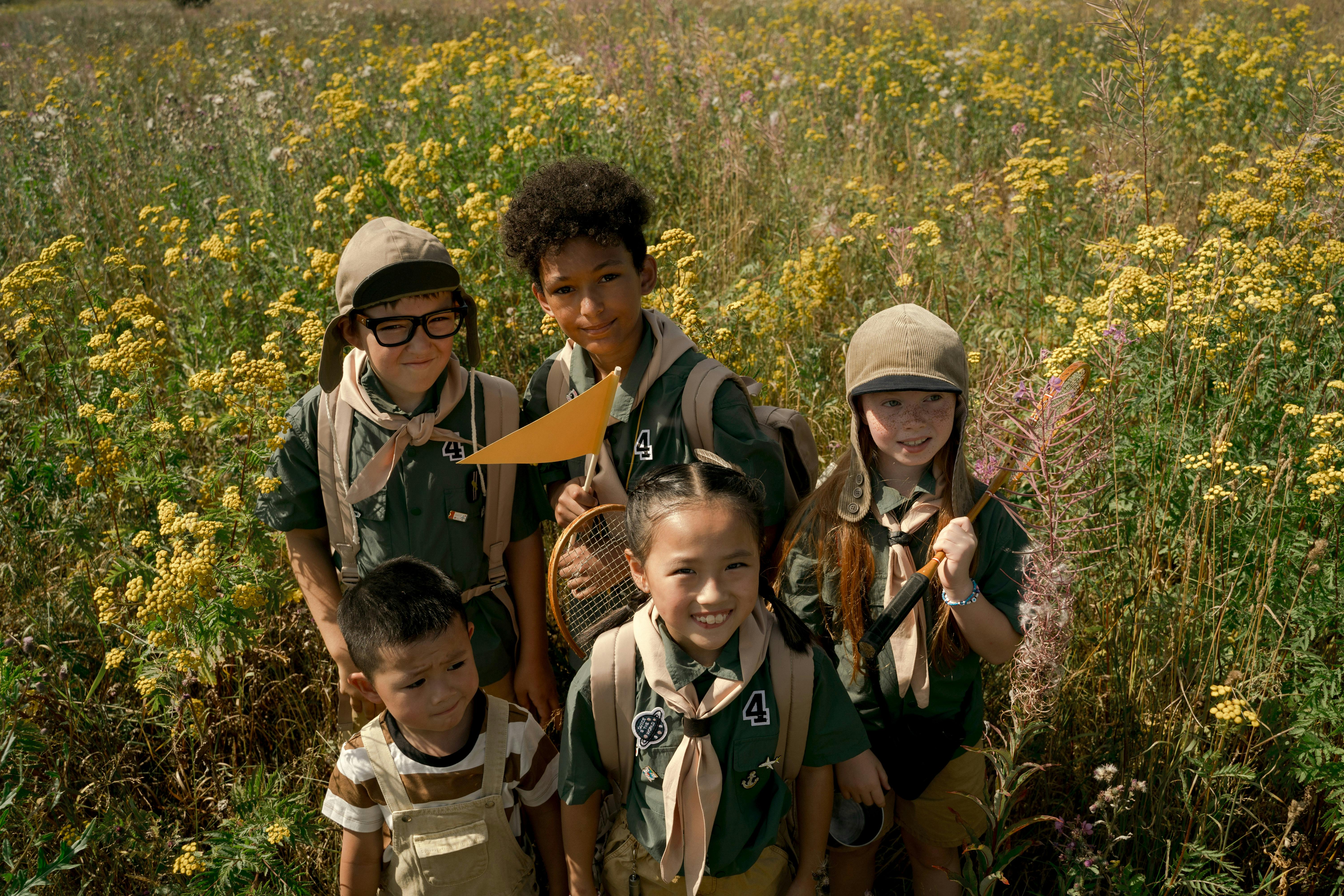 picutre of five children smiling in an open field, one holding a small yellow flag 