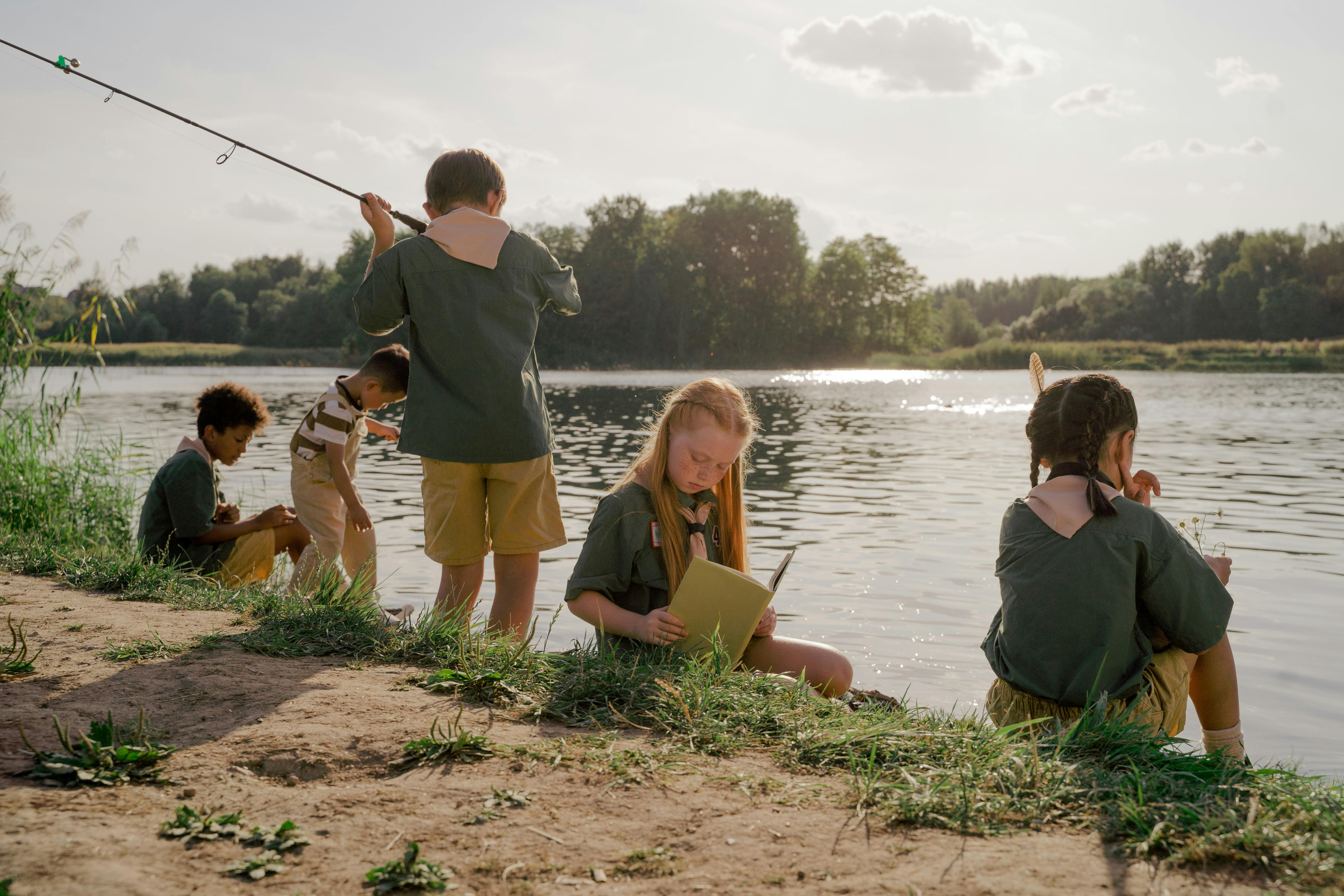 a group of five children by a lake fishing and writing in a book