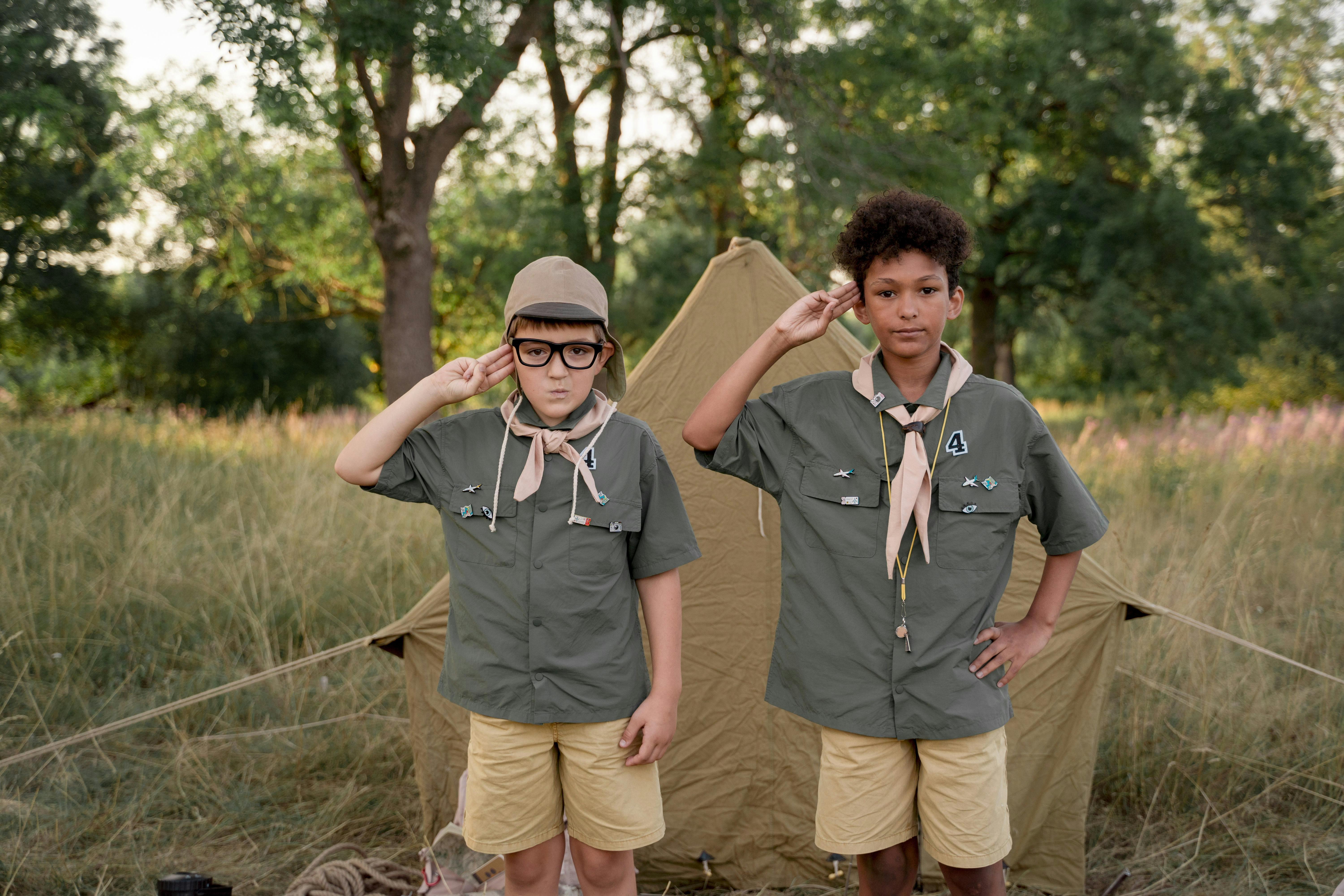 two boys standing in front of a tent in a wood doing the scouts salute